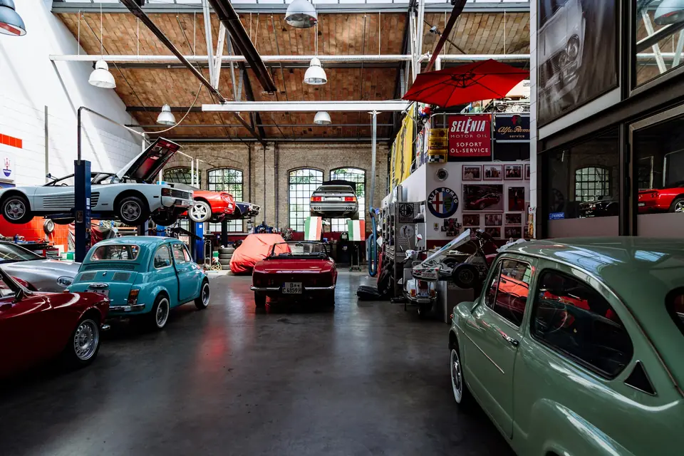 Classic-car workshop in a brick hall with cars on lifts above a dark, sheen-finished concrete floor