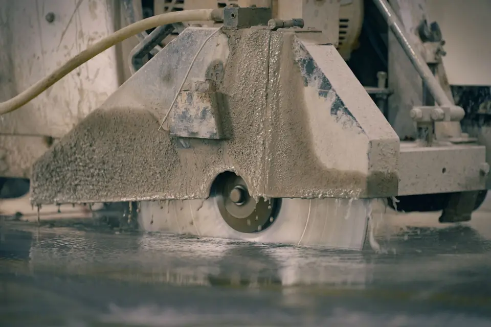 Walk-behind diamond-blade saw wet-cutting a straight line into a concrete floor, covered in gray slurry