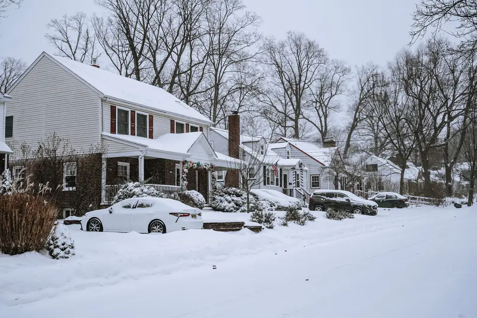 Snow-covered residential street with parked cars buried in snow under an overcast sky