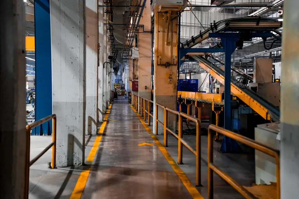 Factory walkway on a dark coated floor marked with yellow safety lines beside orange railings and blue machinery
