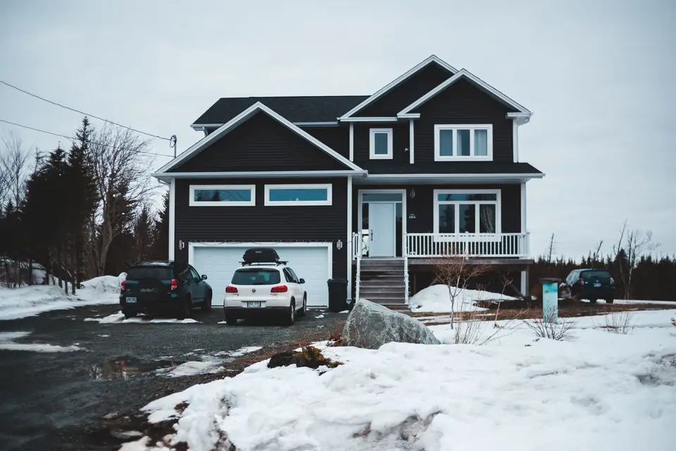 Two-story house with an attached two-car garage, cars parked in a slushy driveway and snow banks in the yard